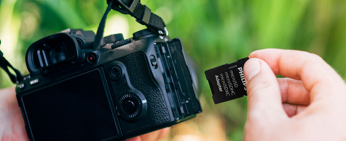 A person holding a camera in one hand and a memory card in the other, ready to capture moments